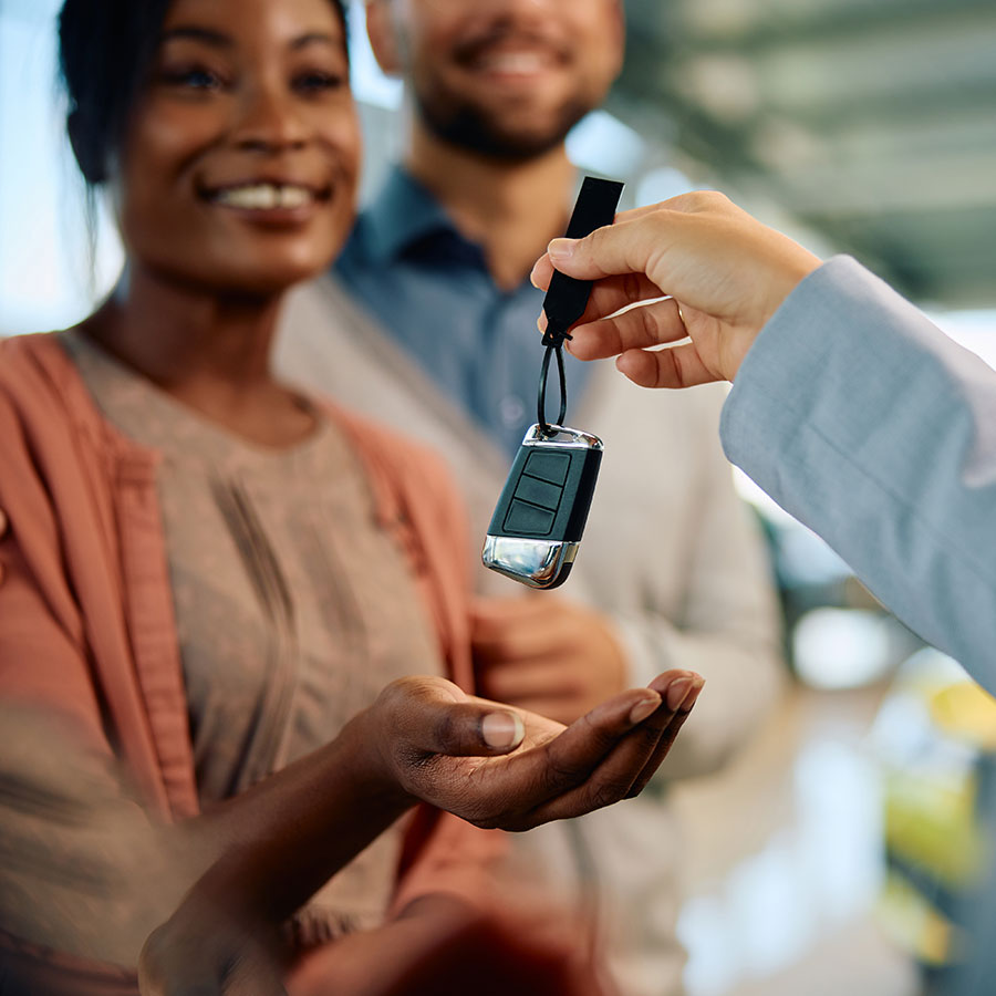 A woman is handed a key to an adventure vehicle that she purchased through an LMG Financing Dealership. She is smiling at the camera, slightly out of focus, while the key and her hand are the center of the image.