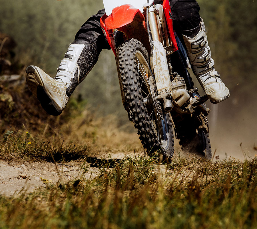 A newly financed dirtbike in action! The focus is on the rider's feet, nearly flying off the pedals as he rounds a dirt corner, wheels spinning in motion.