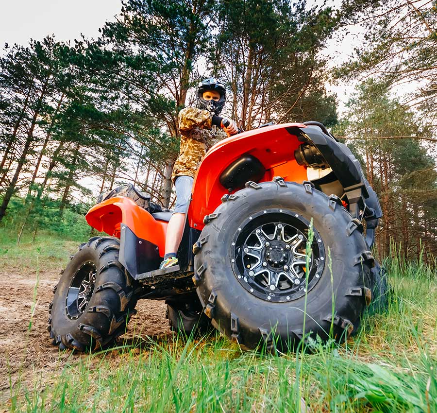 A man is riding a red ATV in the woods, looking intensely down at the camera. He is wearing a helmet and a camo jacket.